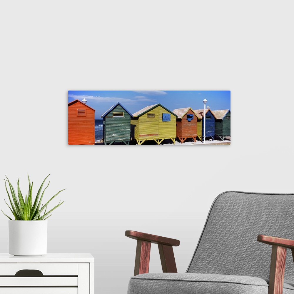 A modern room featuring Panoramic photograph taken of multi-colored huts that line the beach with the ocean viewed in the...