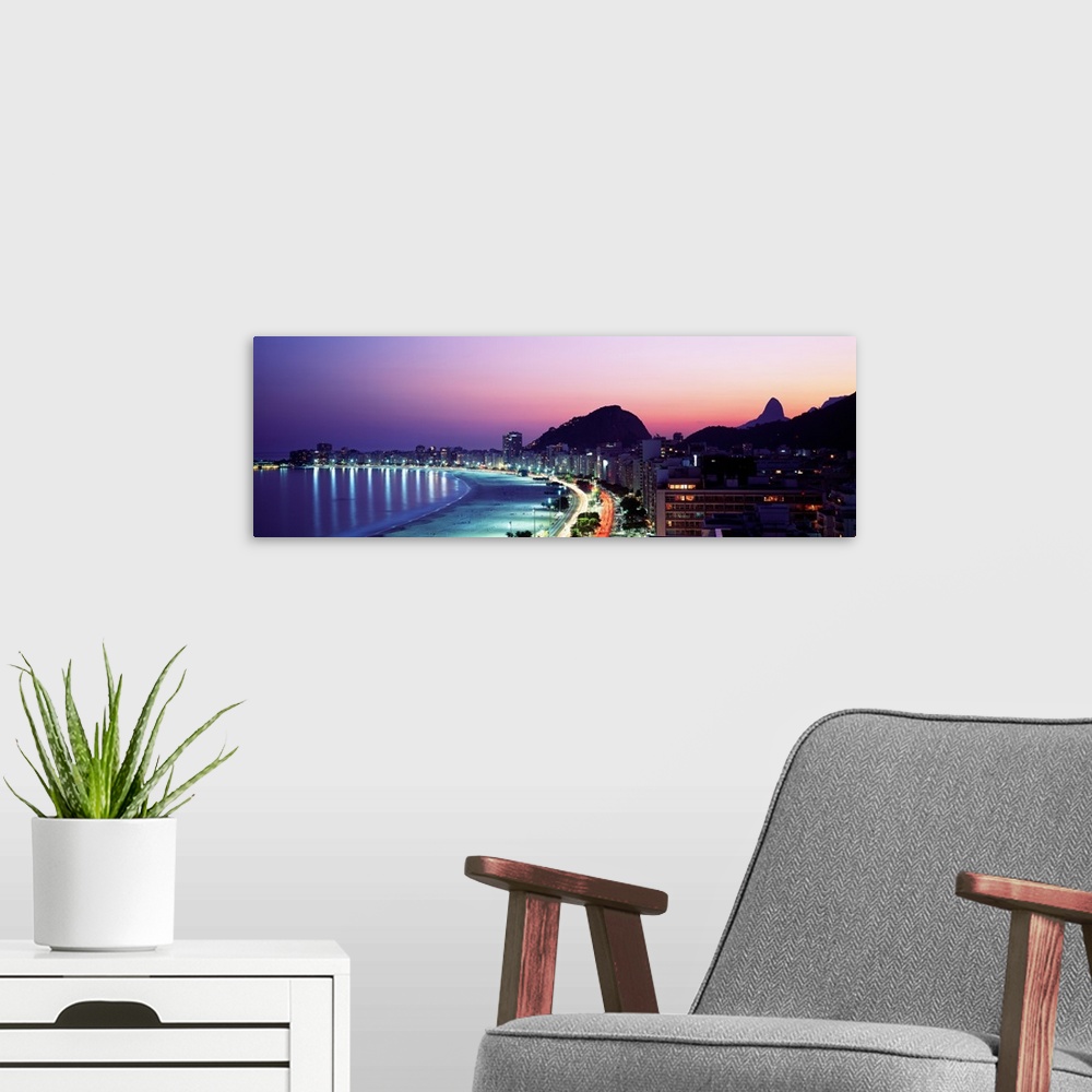 A modern room featuring Panoramic, giant photograph of buildings lit along Copacabana Beach at night, mountains in the ba...