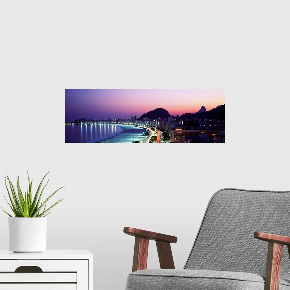 A modern room featuring Panoramic, giant photograph of buildings lit along Copacabana Beach at night, mountains in the ba...