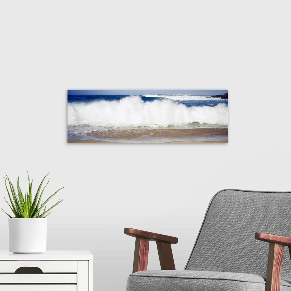 A modern room featuring Panoramic photograph of large waves crashing into the beach, bright blue water in the background,...