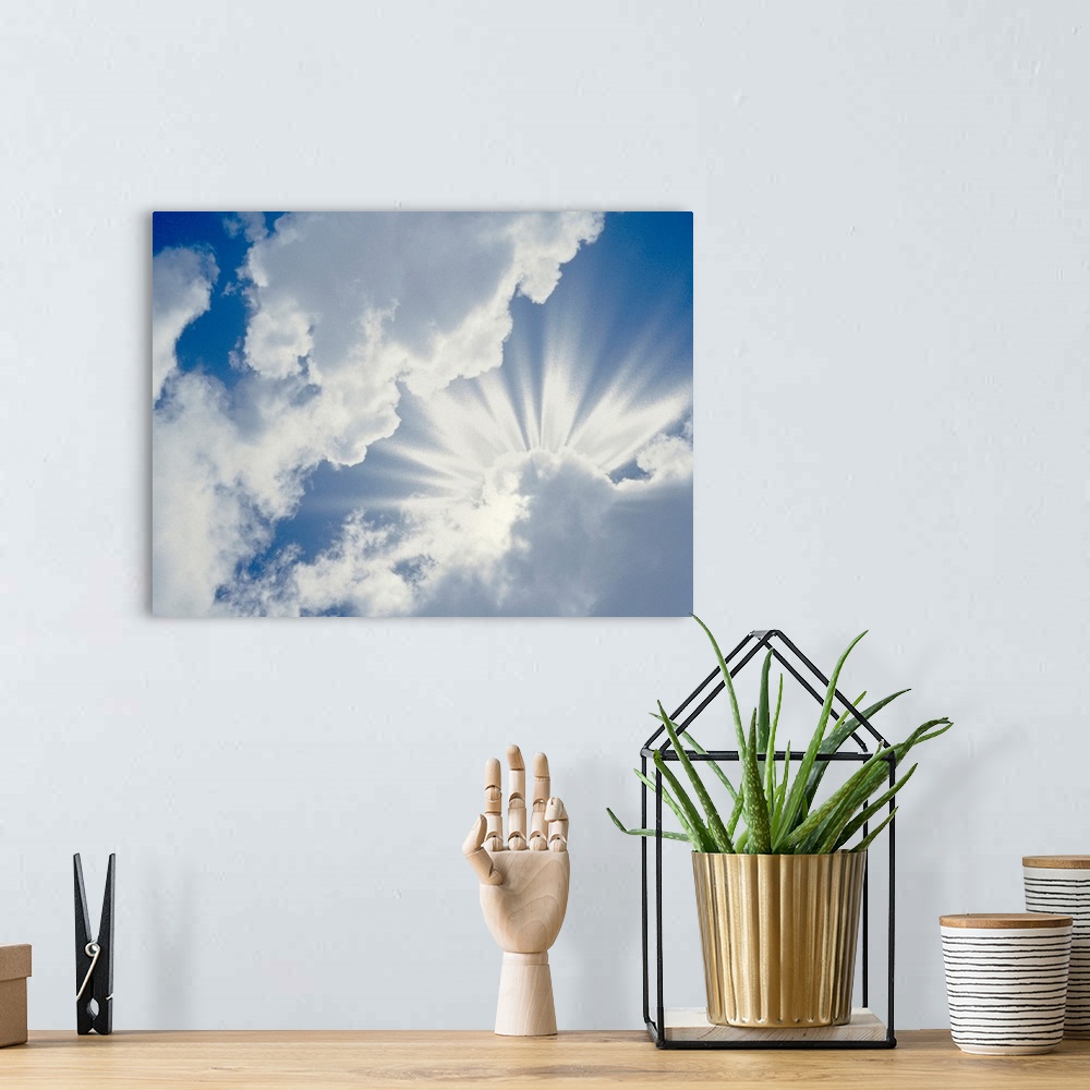 A bohemian room featuring Large photograph of the sky on a cloudy day with the sun's rays about to break through.