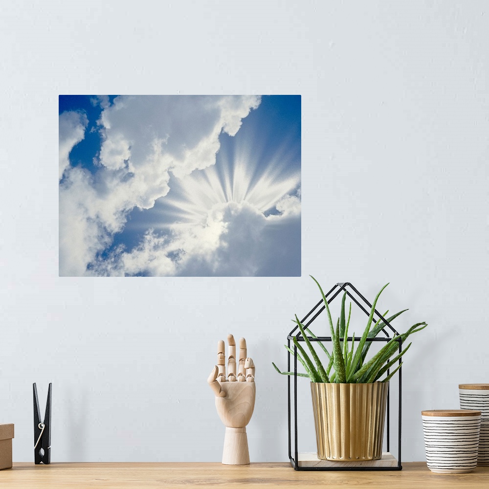 A bohemian room featuring Large photograph of the sky on a cloudy day with the sun's rays about to break through.