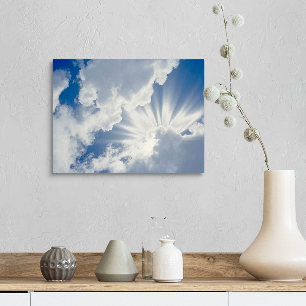 A farmhouse room featuring Large photograph of the sky on a cloudy day with the sun's rays about to break through.