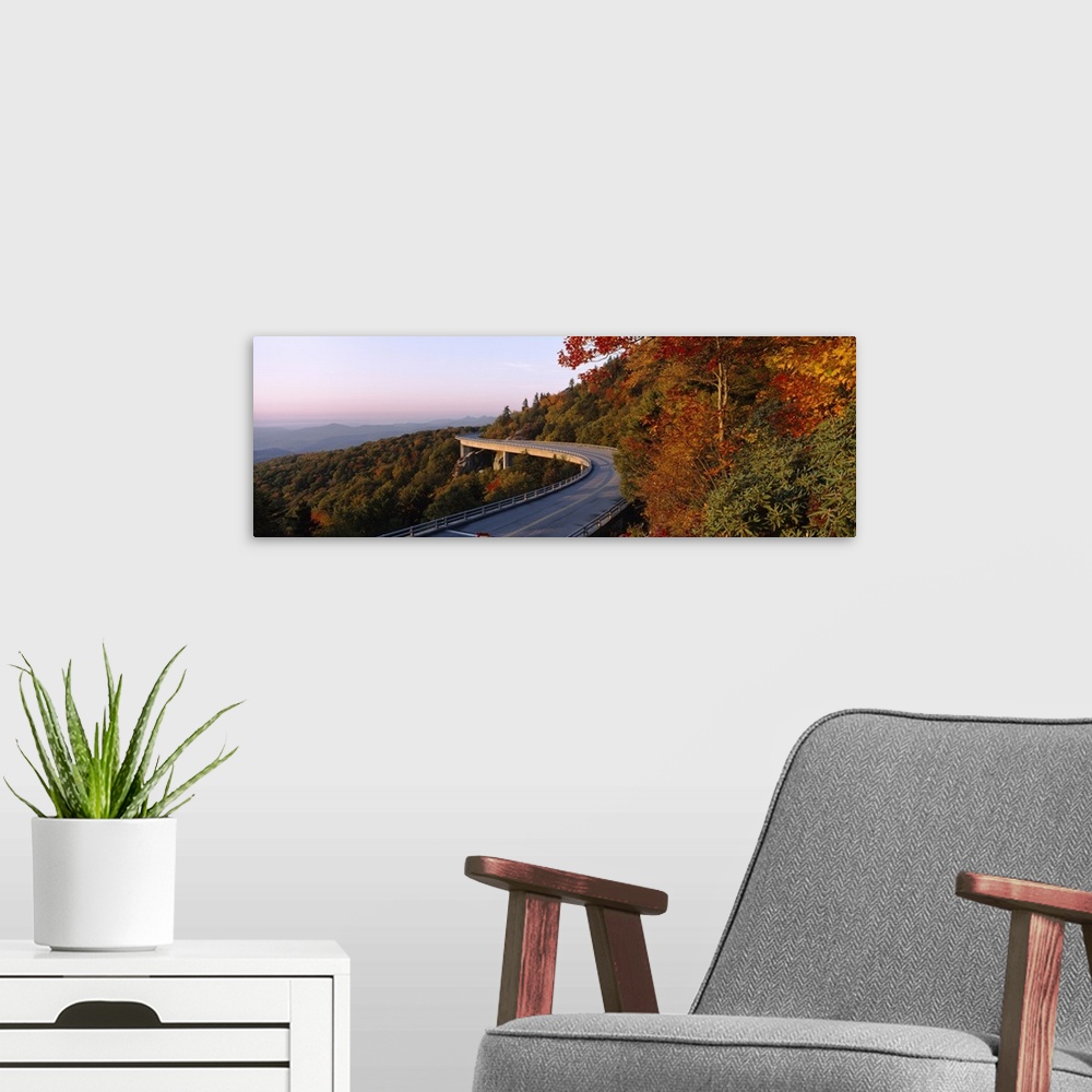A modern room featuring Panoramic photograph of winding mountain road with tree tops below it and mountain silhouette in ...