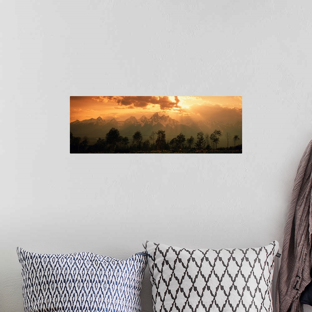 A bohemian room featuring A large panoramic picture of snow topped mountains during a sunset pushed back behind trees and f...