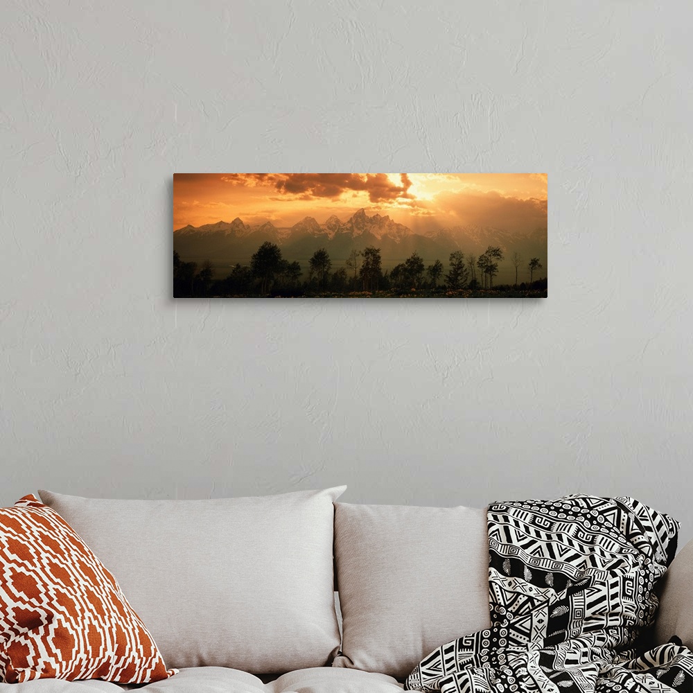 A bohemian room featuring A large panoramic picture of snow topped mountains during a sunset pushed back behind trees and f...