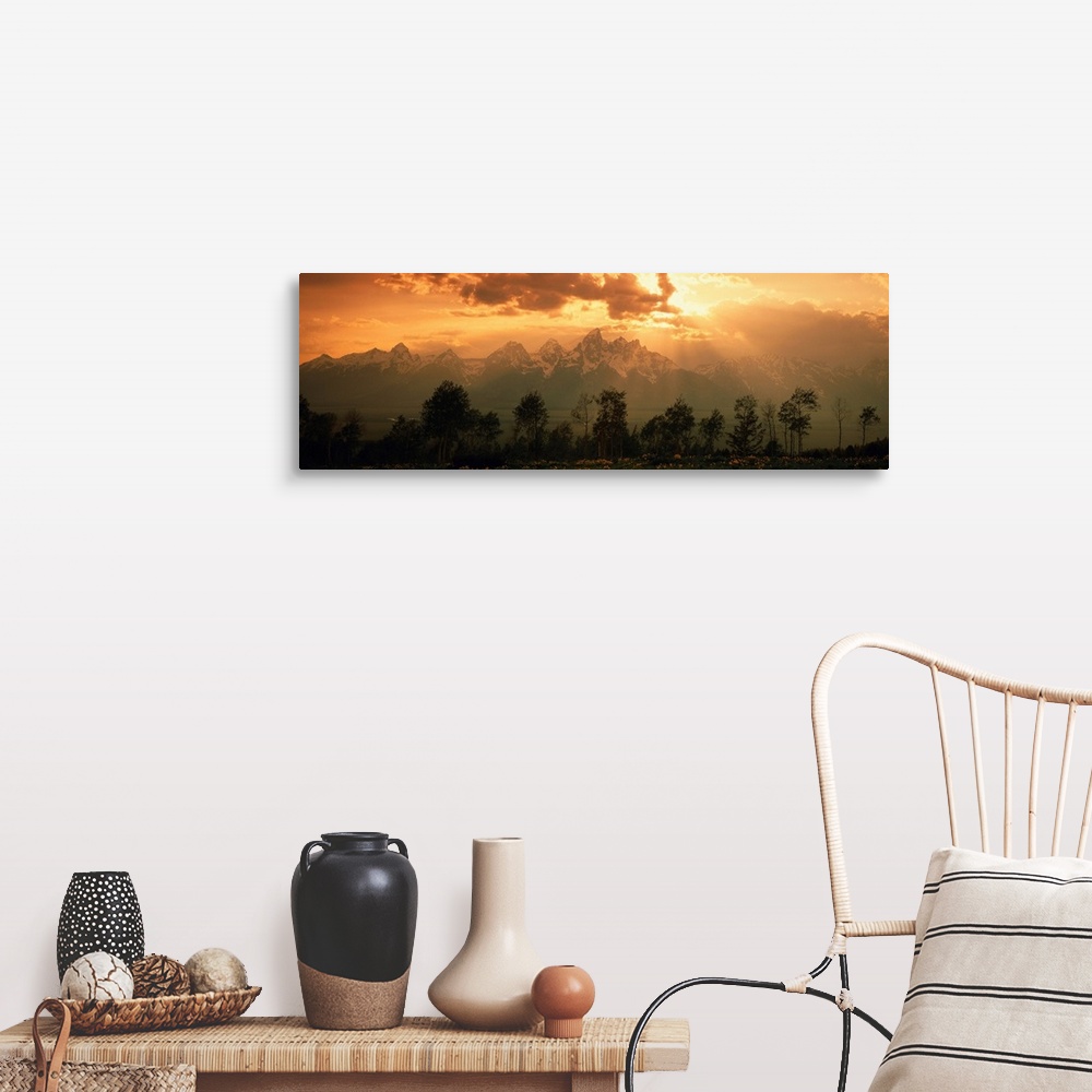 A farmhouse room featuring A large panoramic picture of snow topped mountains during a sunset pushed back behind trees and f...