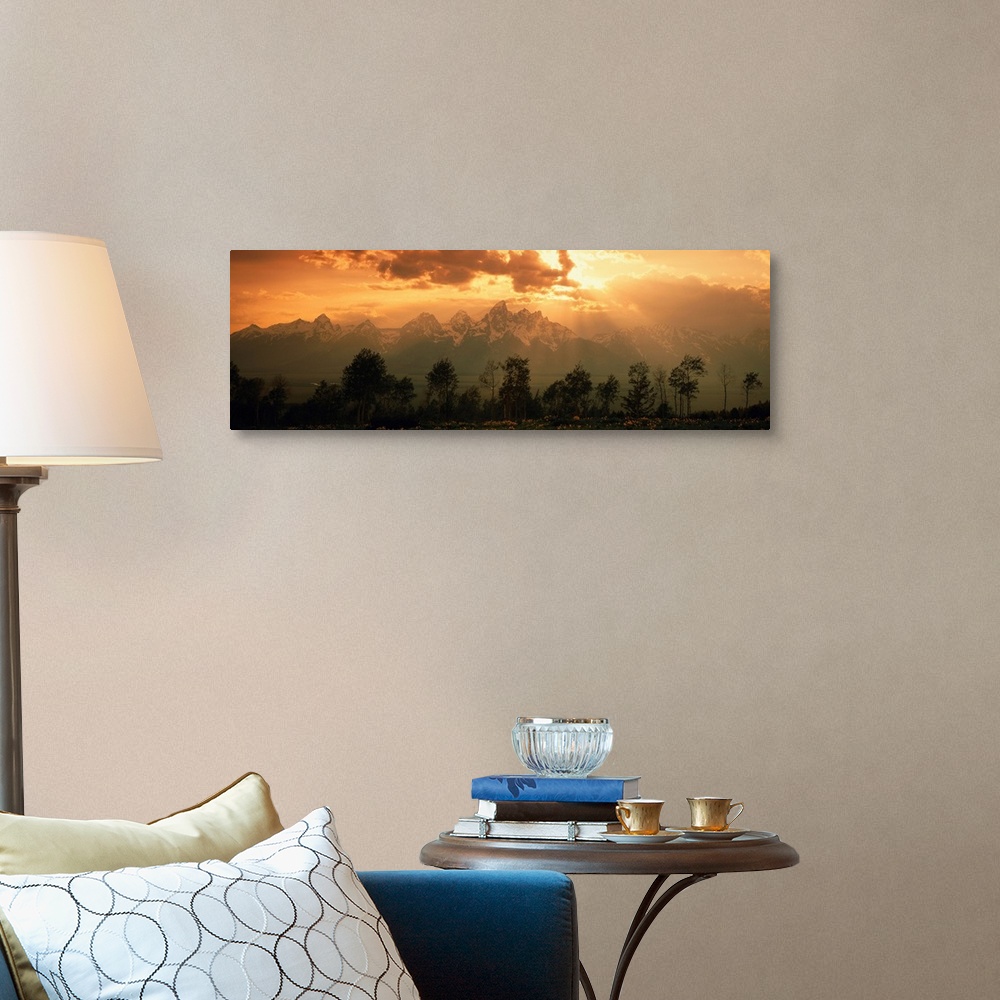 A traditional room featuring A large panoramic picture of snow topped mountains during a sunset pushed back behind trees and f...