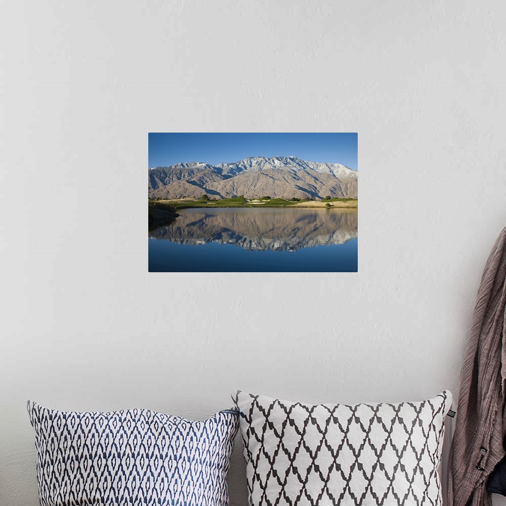 A bohemian room featuring A large mountain range is photographed from across a body of water that it reflects down in.
