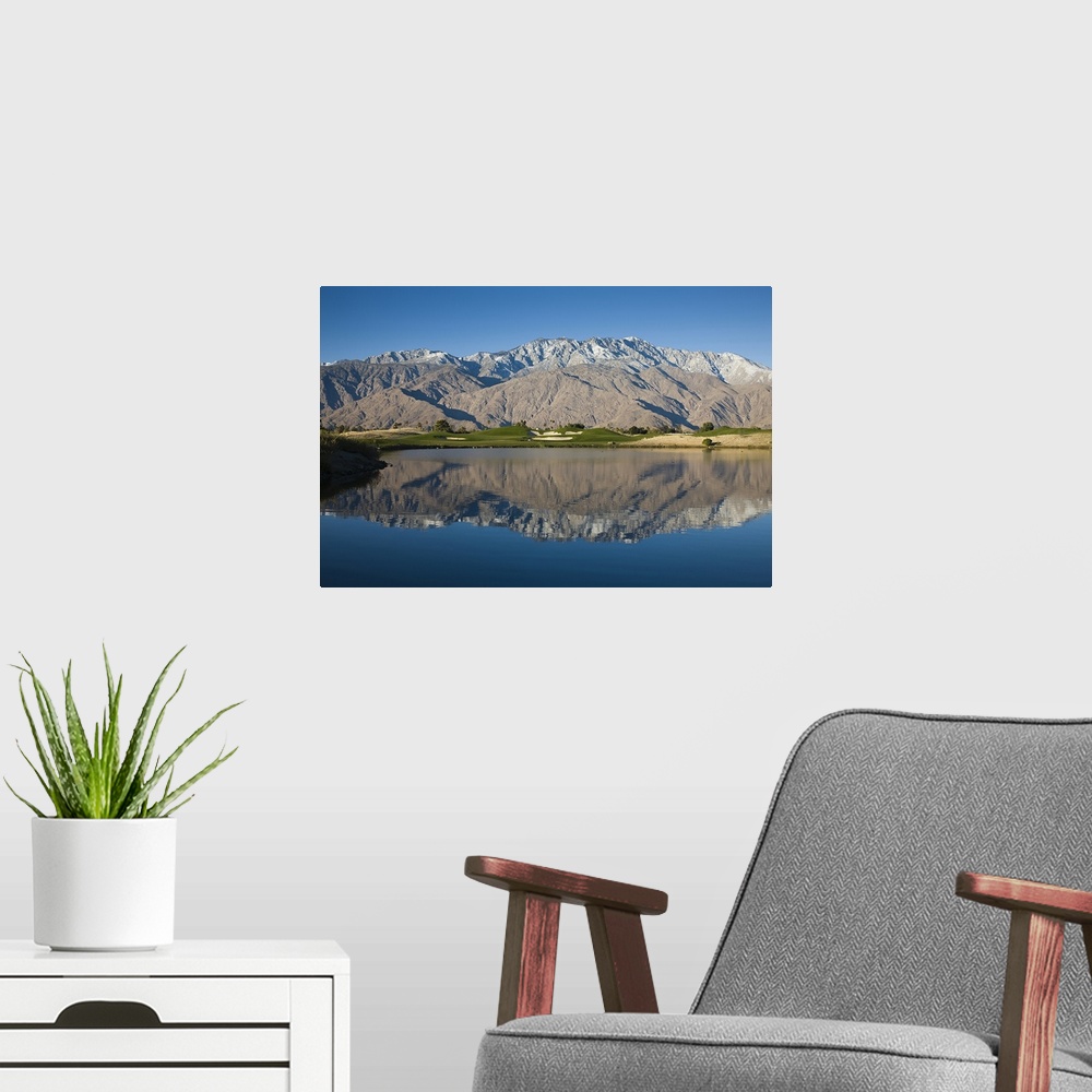 A modern room featuring A large mountain range is photographed from across a body of water that it reflects down in.