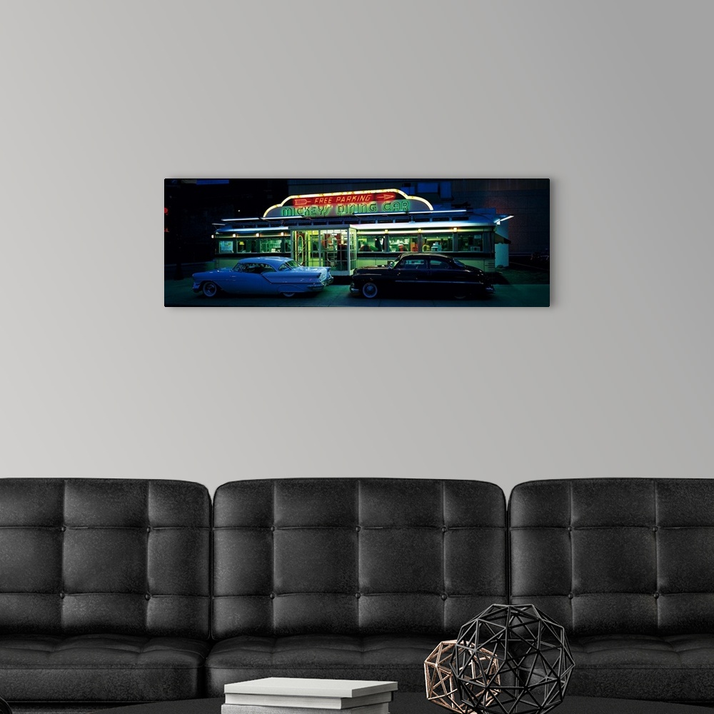 A modern room featuring Panoramic photograph of two vintage cars sitting outside of a lit up eatery at night with neon si...