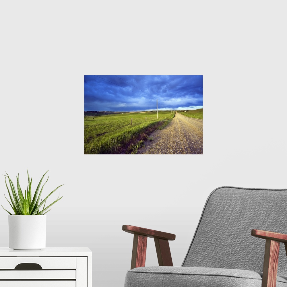 A modern room featuring Landscape, oversized photograph of a gravel road, open fields on wither side, beneath a stormy sk...