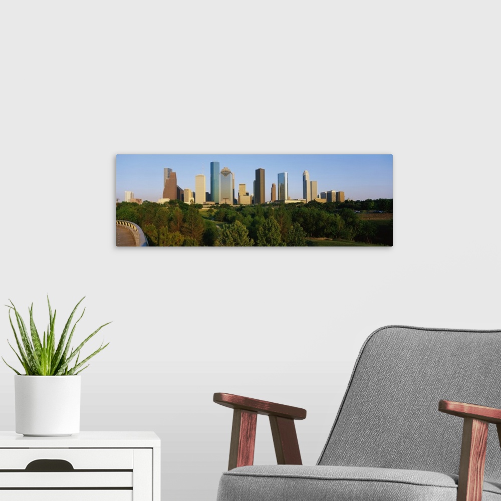 A modern room featuring Skyscrapers in the Houston skyline are photographed from a distance with large trees in the foreg...