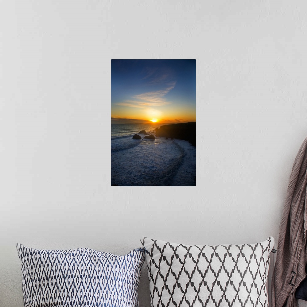 A bohemian room featuring The sun is setting in the distance over the ocean with a large cliff to the right that is silhoue...
