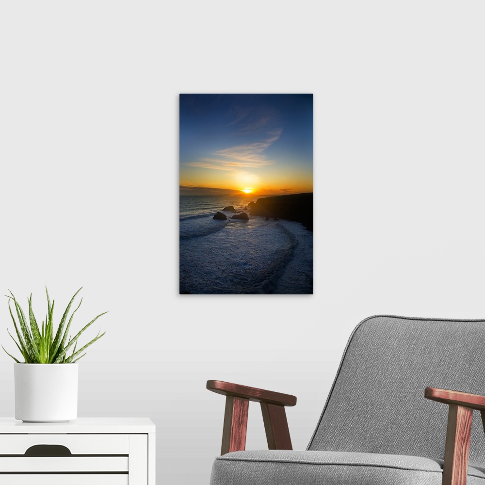 A modern room featuring The sun is setting in the distance over the ocean with a large cliff to the right that is silhoue...