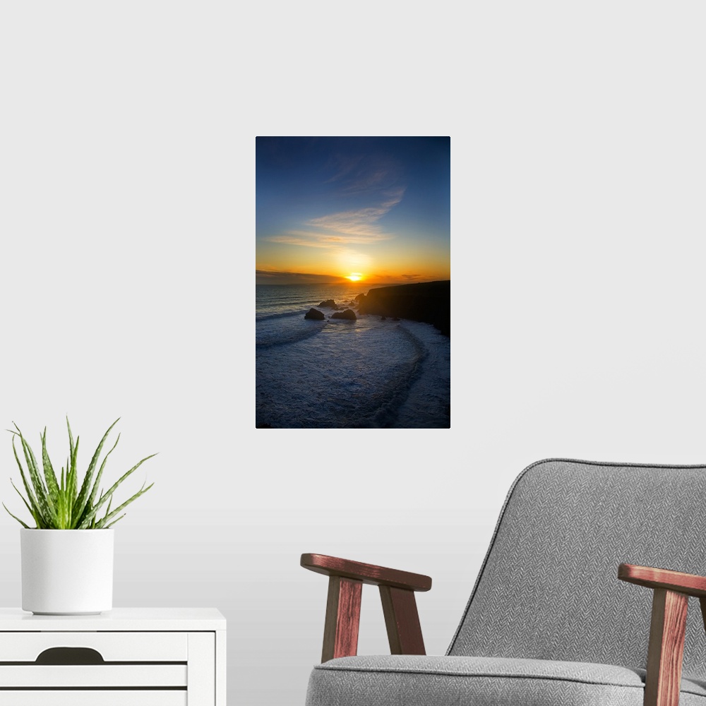 A modern room featuring The sun is setting in the distance over the ocean with a large cliff to the right that is silhoue...