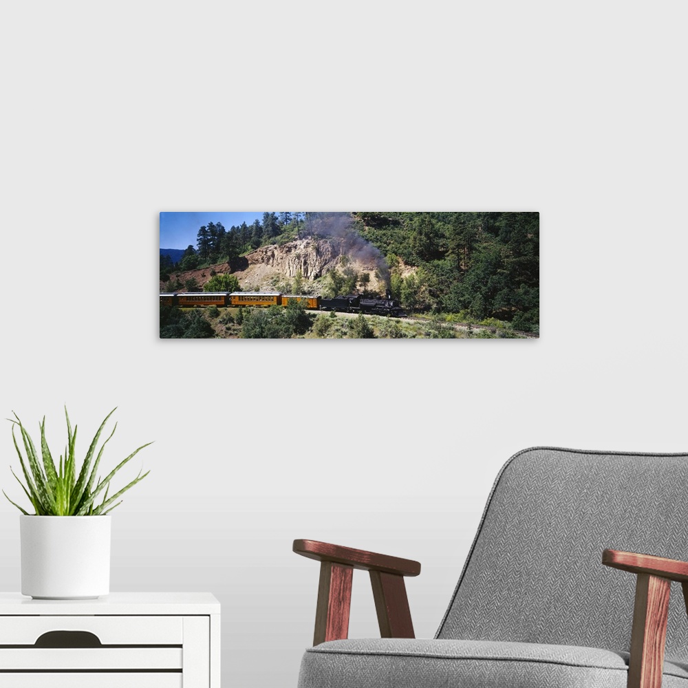 A modern room featuring This is a panoramic photograph of a vintage engine and train cars passing through the mountains o...