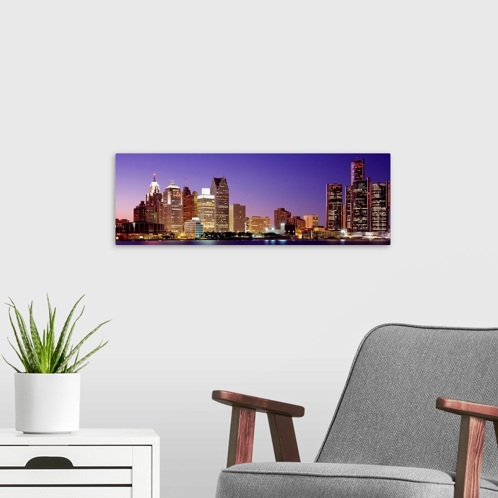 A modern room featuring A panoramic cityscape at dusk with lights illuminated the buildings and water.