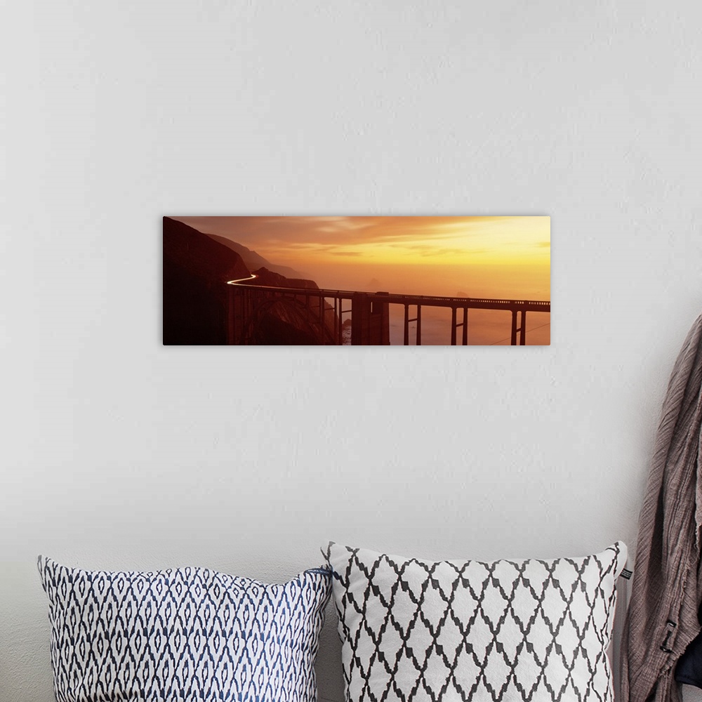 A bohemian room featuring Panoramic photograph of overpass winding through mountains over the ocean at sunset.