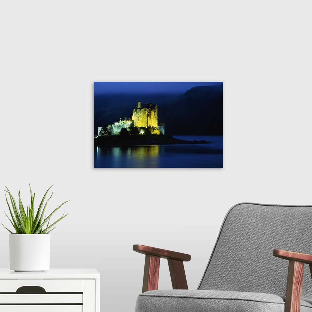 A modern room featuring Eilean Donan Castle illuminated at night, water reflection, Conchra, Scotland.
