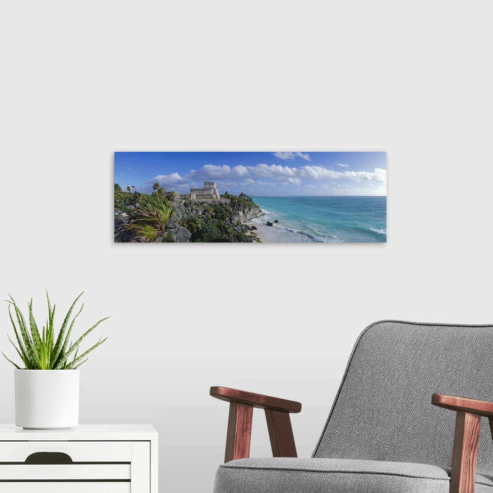 A modern room featuring Large panoramic piece of ruins on a cliff off the coast of Mexico. Foliage and rocks are seen clo...