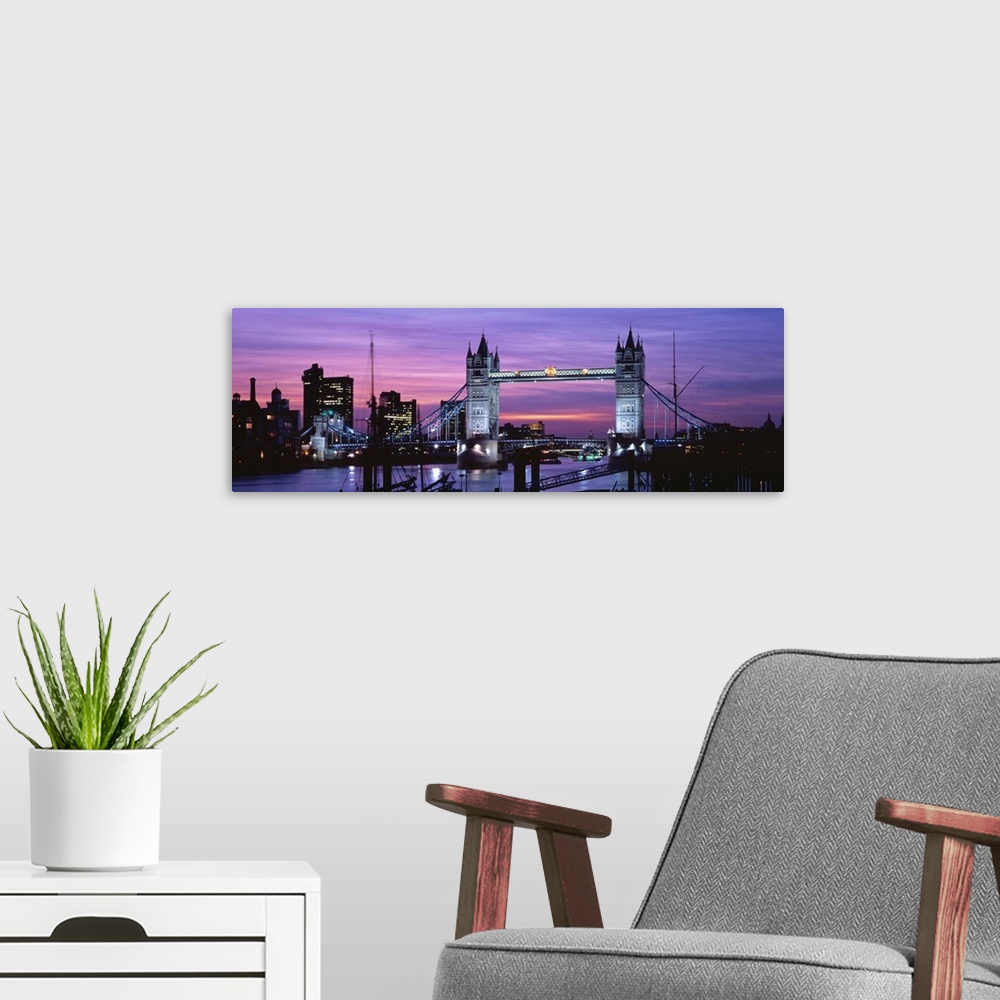 A modern room featuring Panoramic view of London's cityscape and the Tower Bridge in front of a pink and purple toned sun...