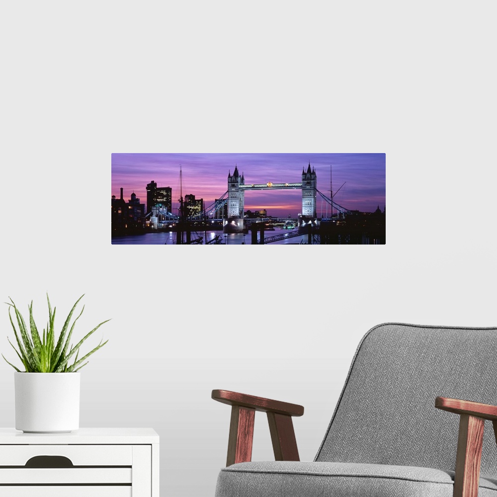 A modern room featuring Panoramic view of London's cityscape and the Tower Bridge in front of a pink and purple toned sun...