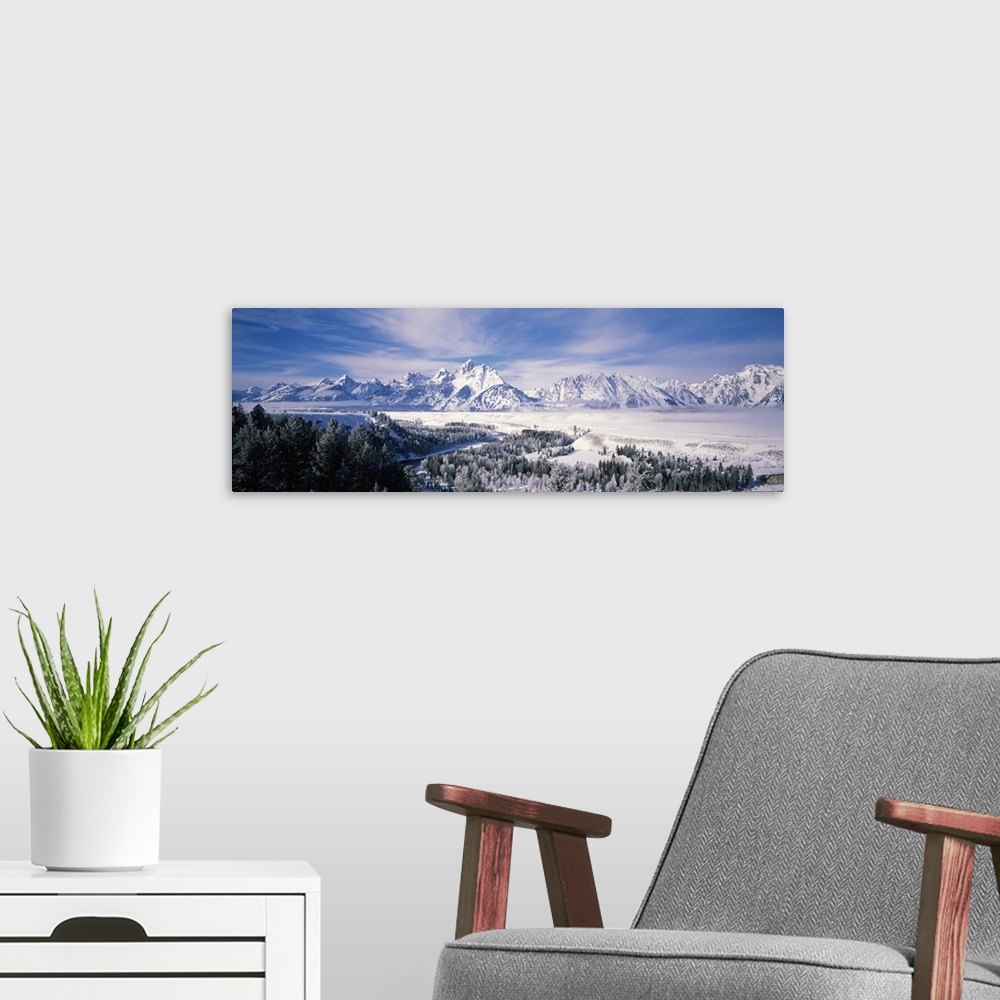 A modern room featuring Panoramic photograph of snow covered mountains with forest in the foreground under a cloudy sky .