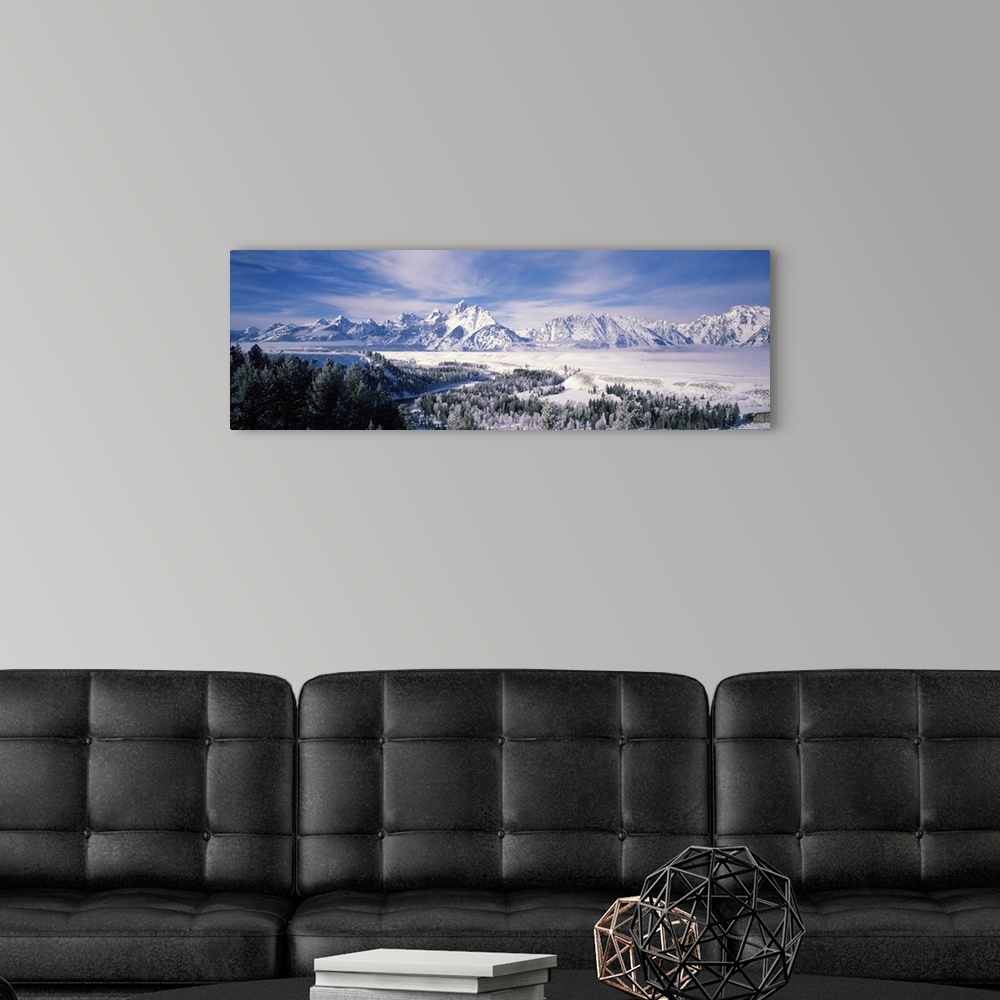 A modern room featuring Panoramic photograph of snow covered mountains with forest in the foreground under a cloudy sky .