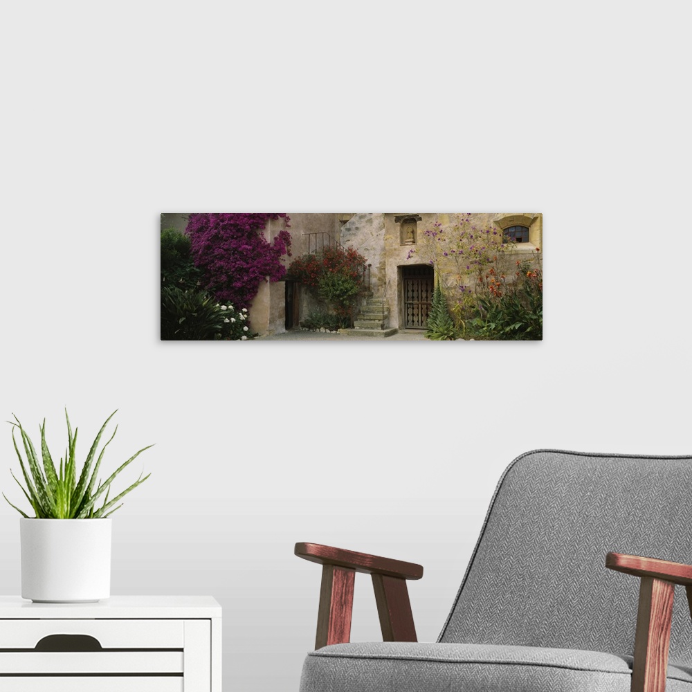 A modern room featuring Panoramic image of an Italian style stone house with large flowering bushes crawling up the side ...