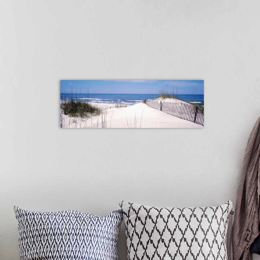 A bohemian room featuring This panoramic photograph looks out to a calm sea over a dune covered in sea grass and a buried f...