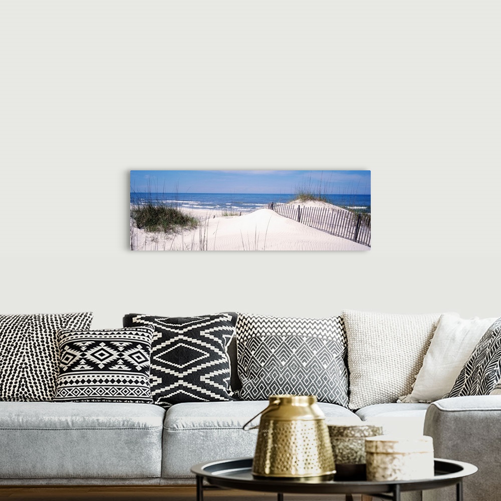 A bohemian room featuring This panoramic photograph looks out to a calm sea over a dune covered in sea grass and a buried f...