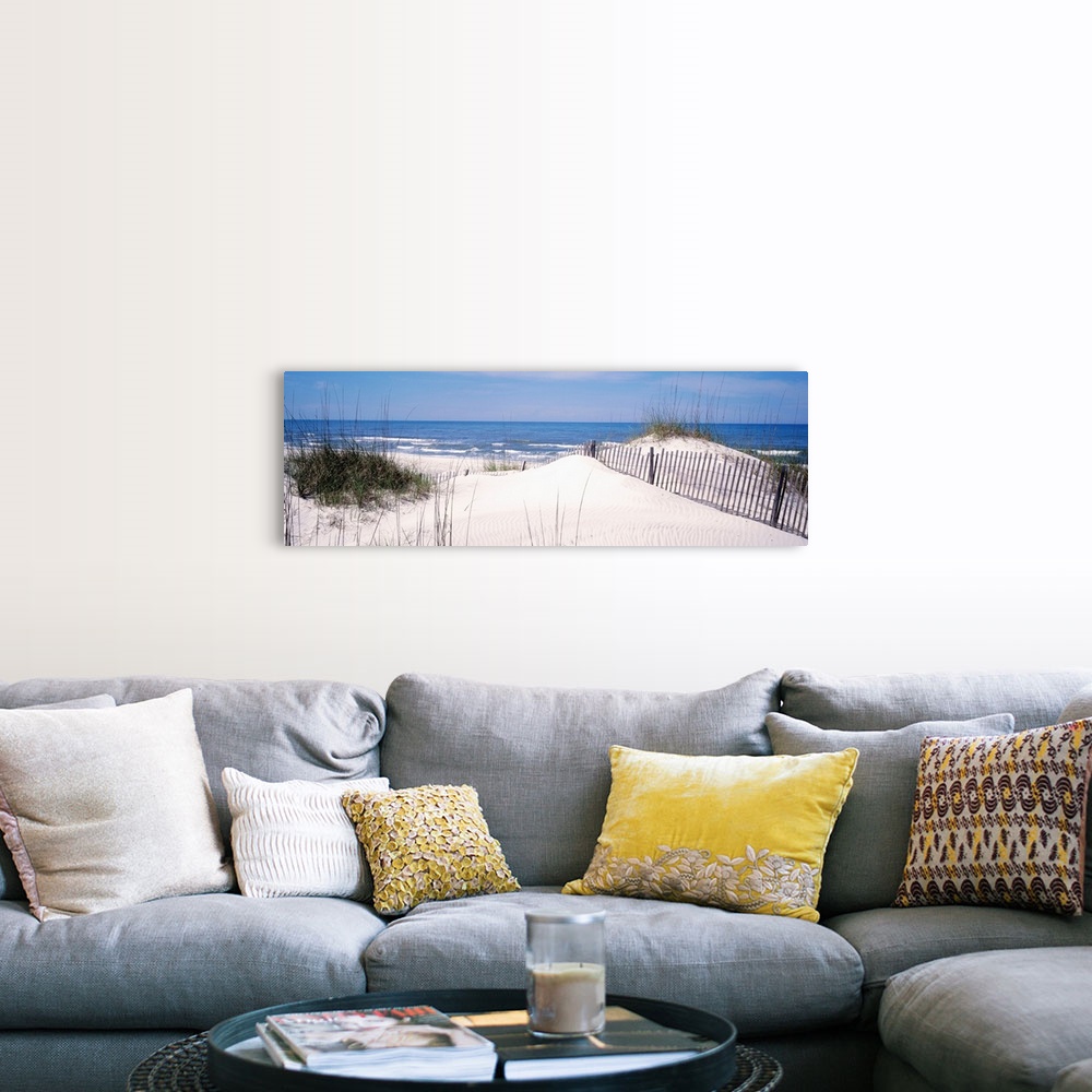 A farmhouse room featuring This panoramic photograph looks out to a calm sea over a dune covered in sea grass and a buried f...