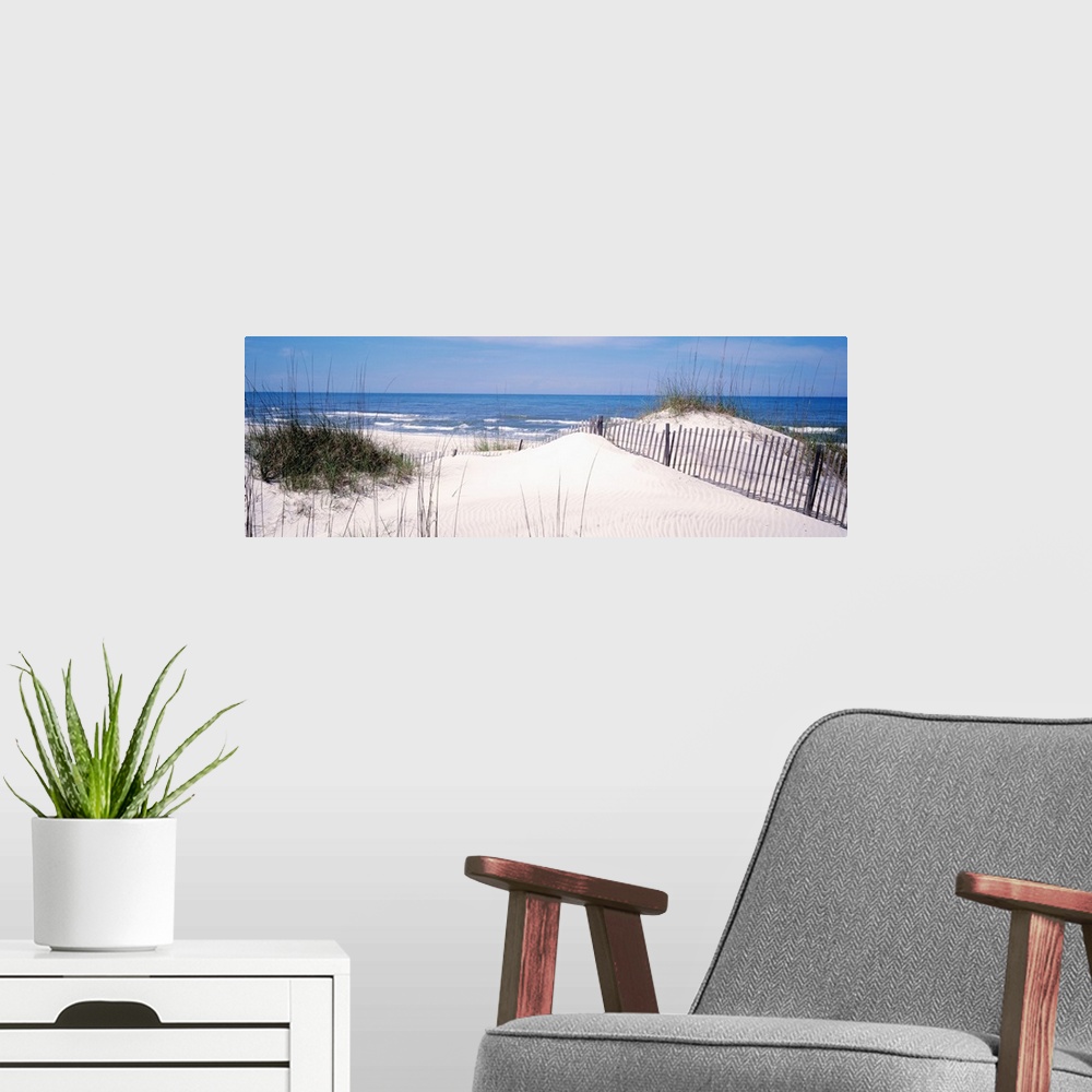 A modern room featuring This panoramic photograph looks out to a calm sea over a dune covered in sea grass and a buried f...