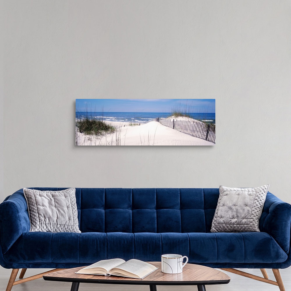 A modern room featuring This panoramic photograph looks out to a calm sea over a dune covered in sea grass and a buried f...