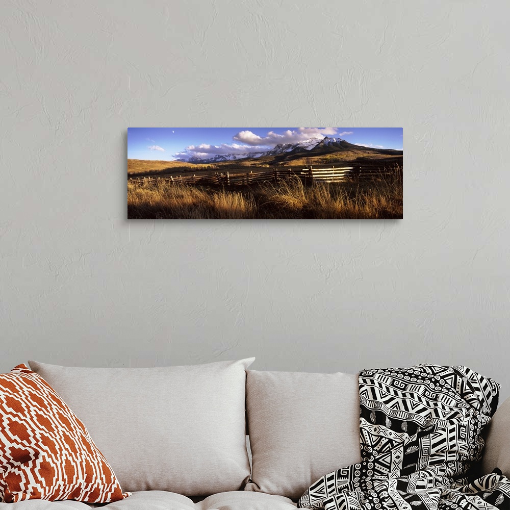 A bohemian room featuring A large panoramic picture of Colorado mountains with a fence and tall grass in the foreground.