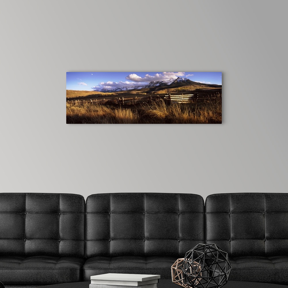A modern room featuring A large panoramic picture of Colorado mountains with a fence and tall grass in the foreground.