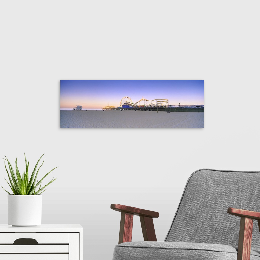 A modern room featuring This is a panoramic photograph of a board walk carnival taken from a sandy beach at twilight.