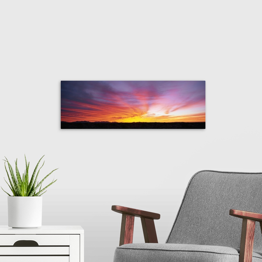 A modern room featuring The strip of land at the bottom of this piece is silhouetted by the beautiful sunset that has dip...