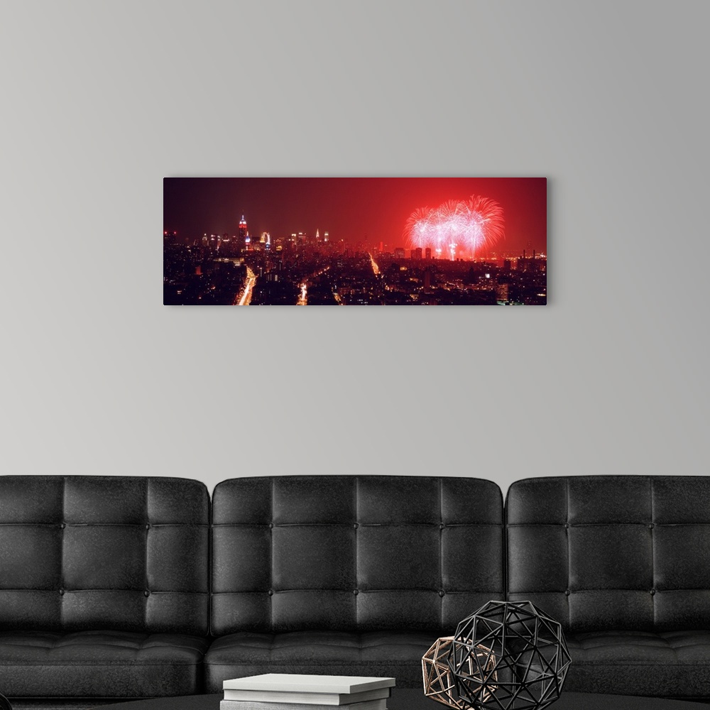 A modern room featuring This glowing panoramic wall art captures the burst of three rockets over the water as well as sev...