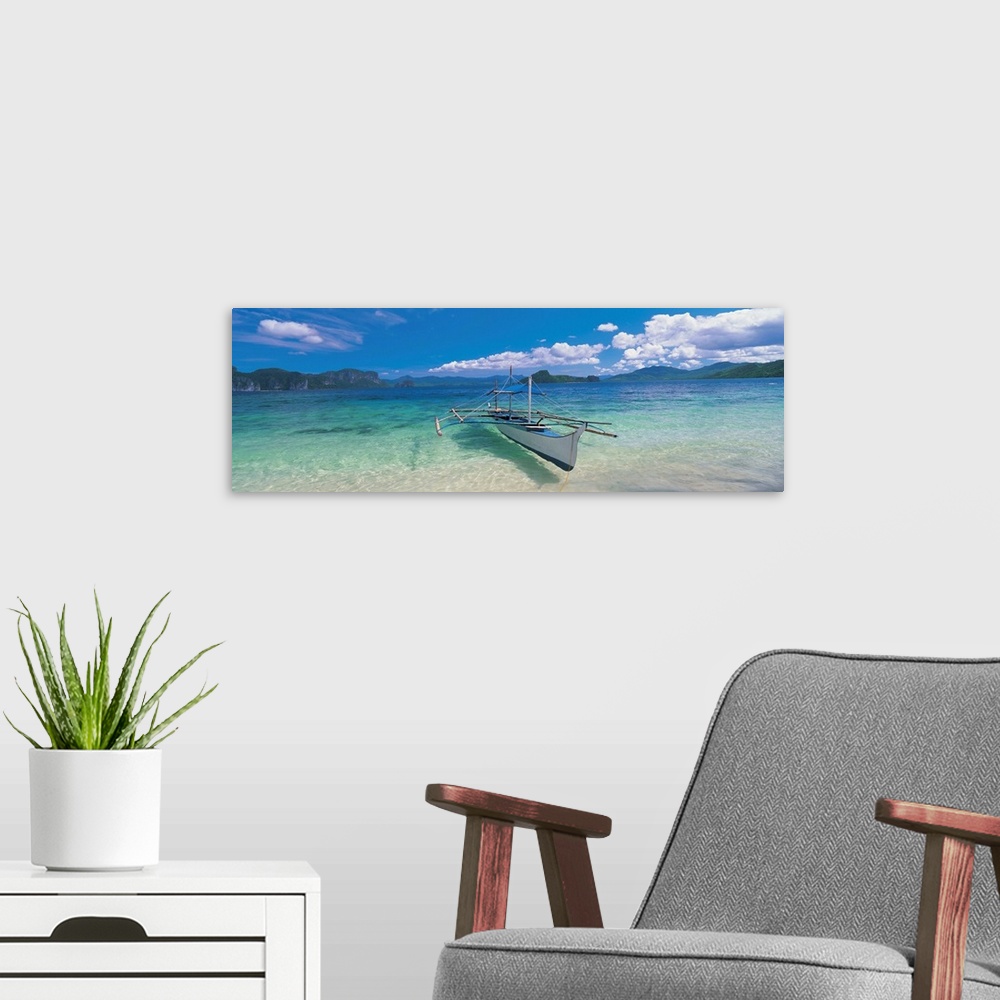 A modern room featuring Panoramic photograph of a canoe atop crystal clear waters with tree covered mountains and cliffs ...