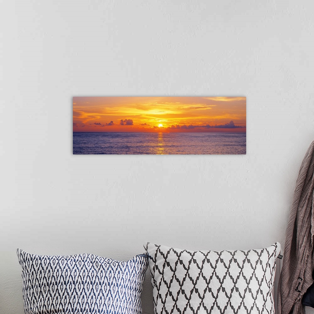 A bohemian room featuring This panoramic seascape shows the sun setting behind clouds on the horizon in this photographic a...
