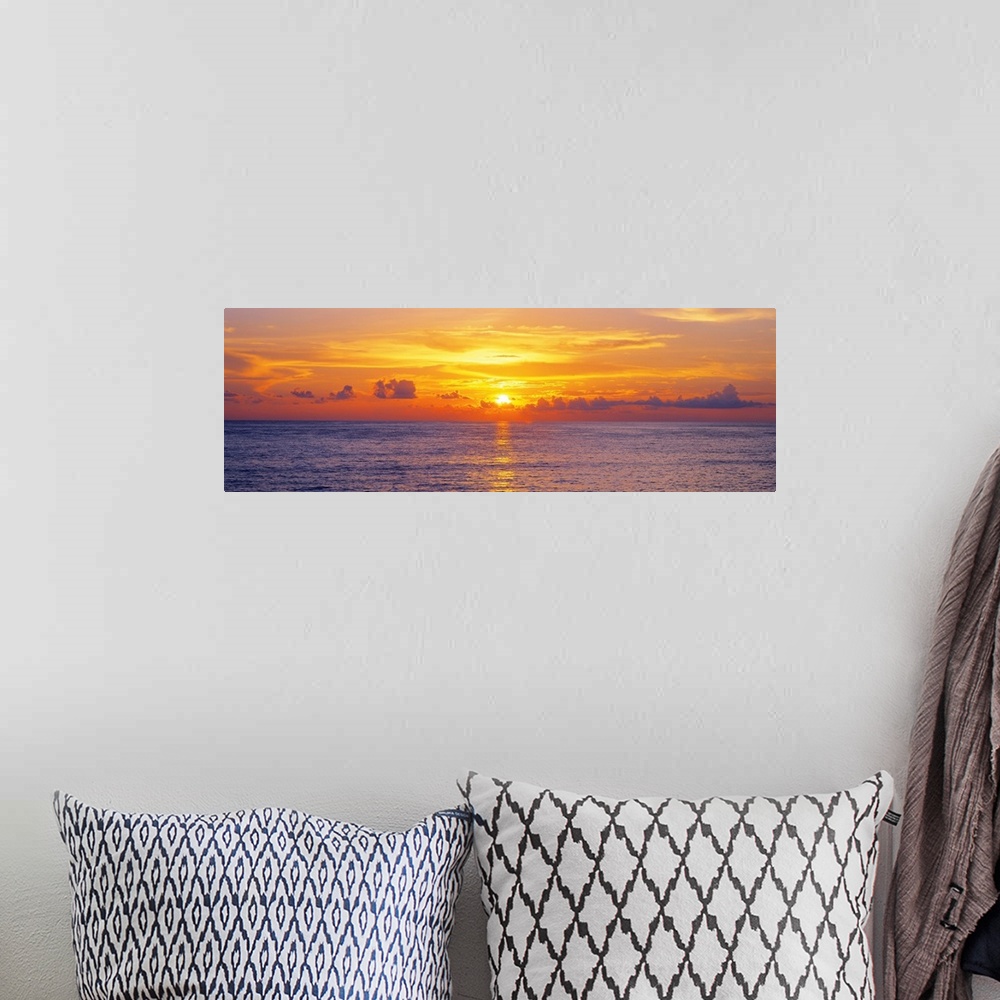 A bohemian room featuring This panoramic seascape shows the sun setting behind clouds on the horizon in this photographic a...