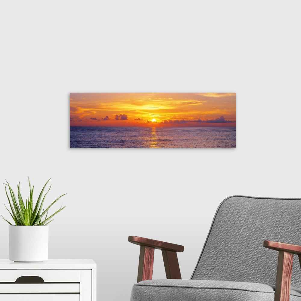 A modern room featuring This panoramic seascape shows the sun setting behind clouds on the horizon in this photographic a...