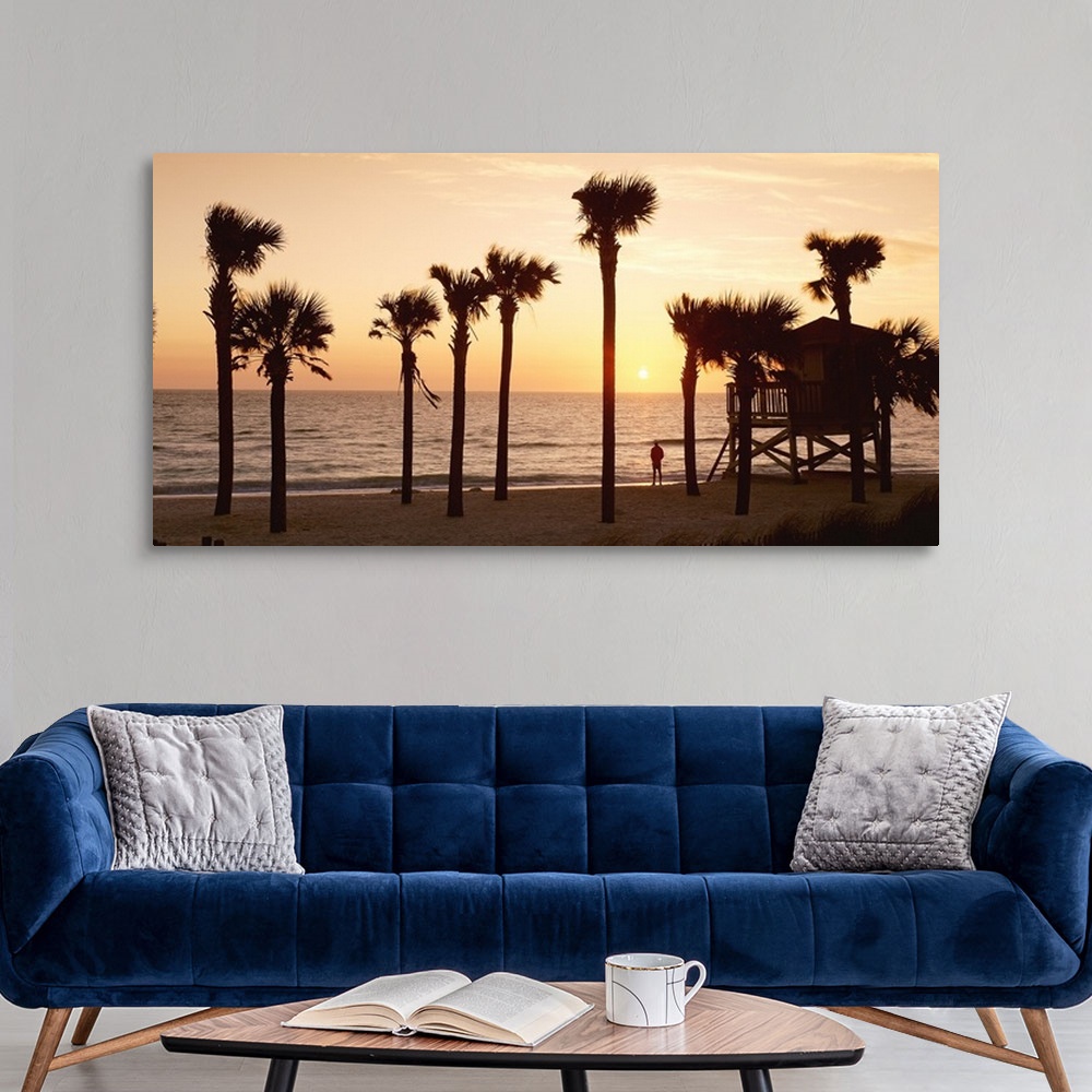 A modern room featuring Panoramic photo of palm trees lining a beach with a man standing on the shore looking out into th...