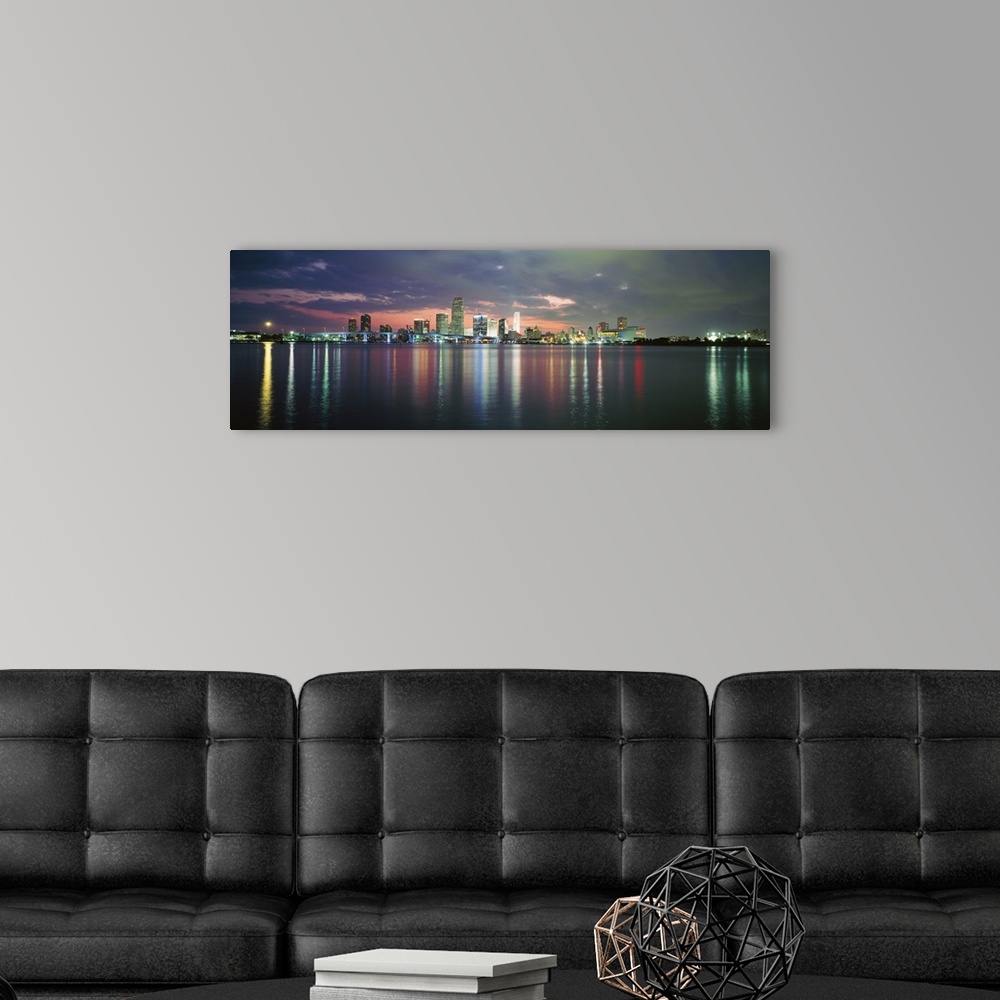 A modern room featuring This city scape photograph shows the city from a distance reflecting on the water on panoramic sh...