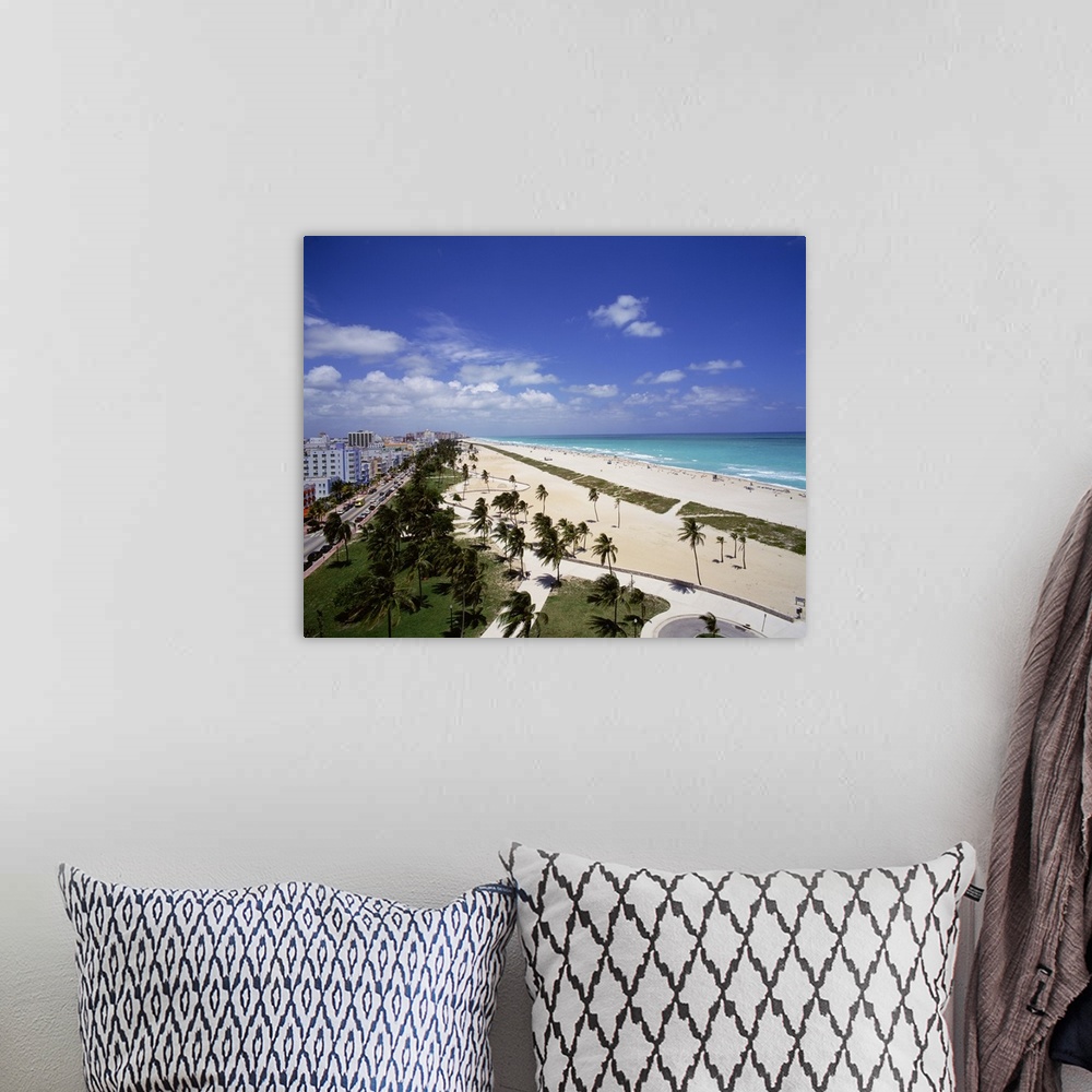 A bohemian room featuring Canvas photo art of a city and street on the left meeting white sand and ocean on the right with ...