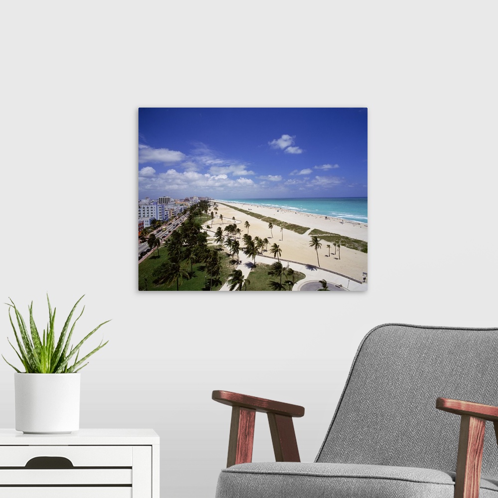 A modern room featuring Canvas photo art of a city and street on the left meeting white sand and ocean on the right with ...