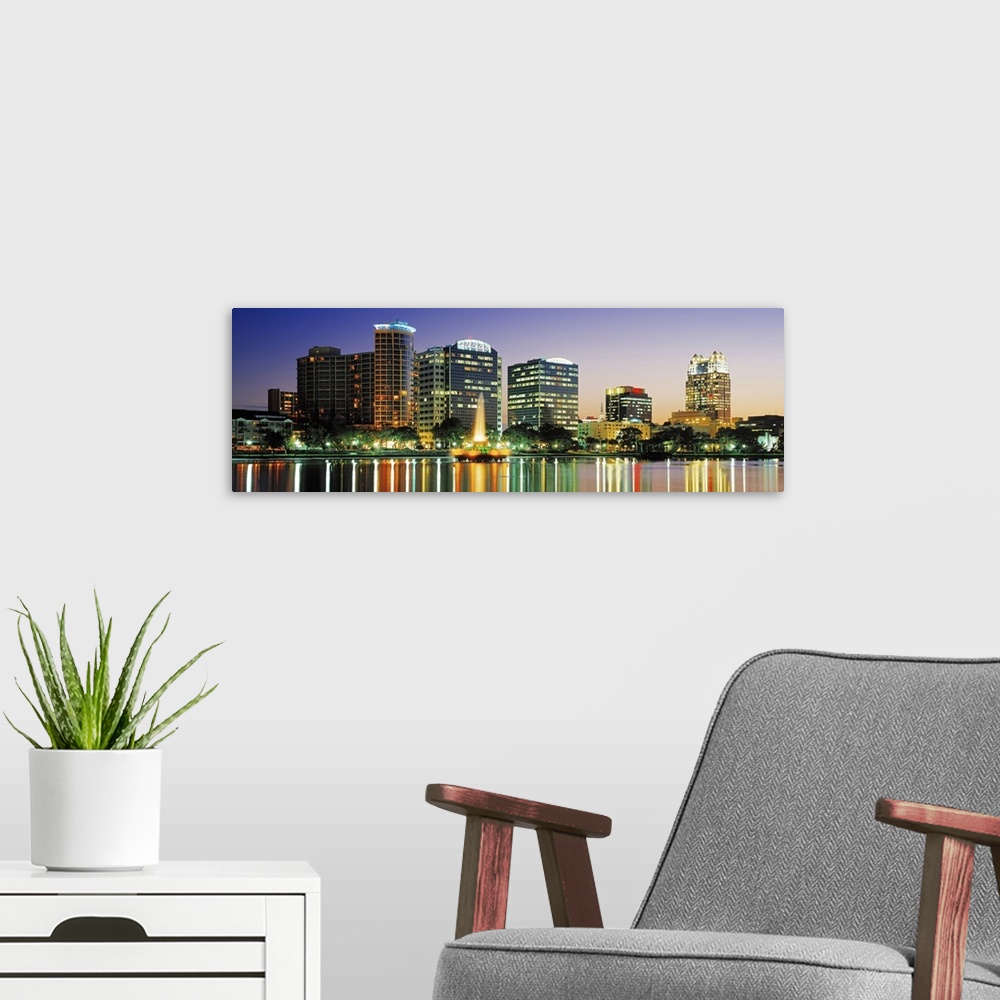 A modern room featuring The Orlando skyline is pictured in panoramic view with the buildings illuminated under an evening...