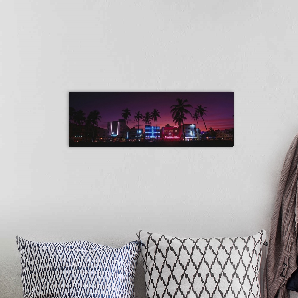 A bohemian room featuring A panoramic canvas of neon lights on art deco buildings on the shore front lined with palm trees.